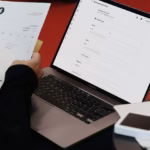 Freelancer checking printed invoices next to a laptop showing an invoice form