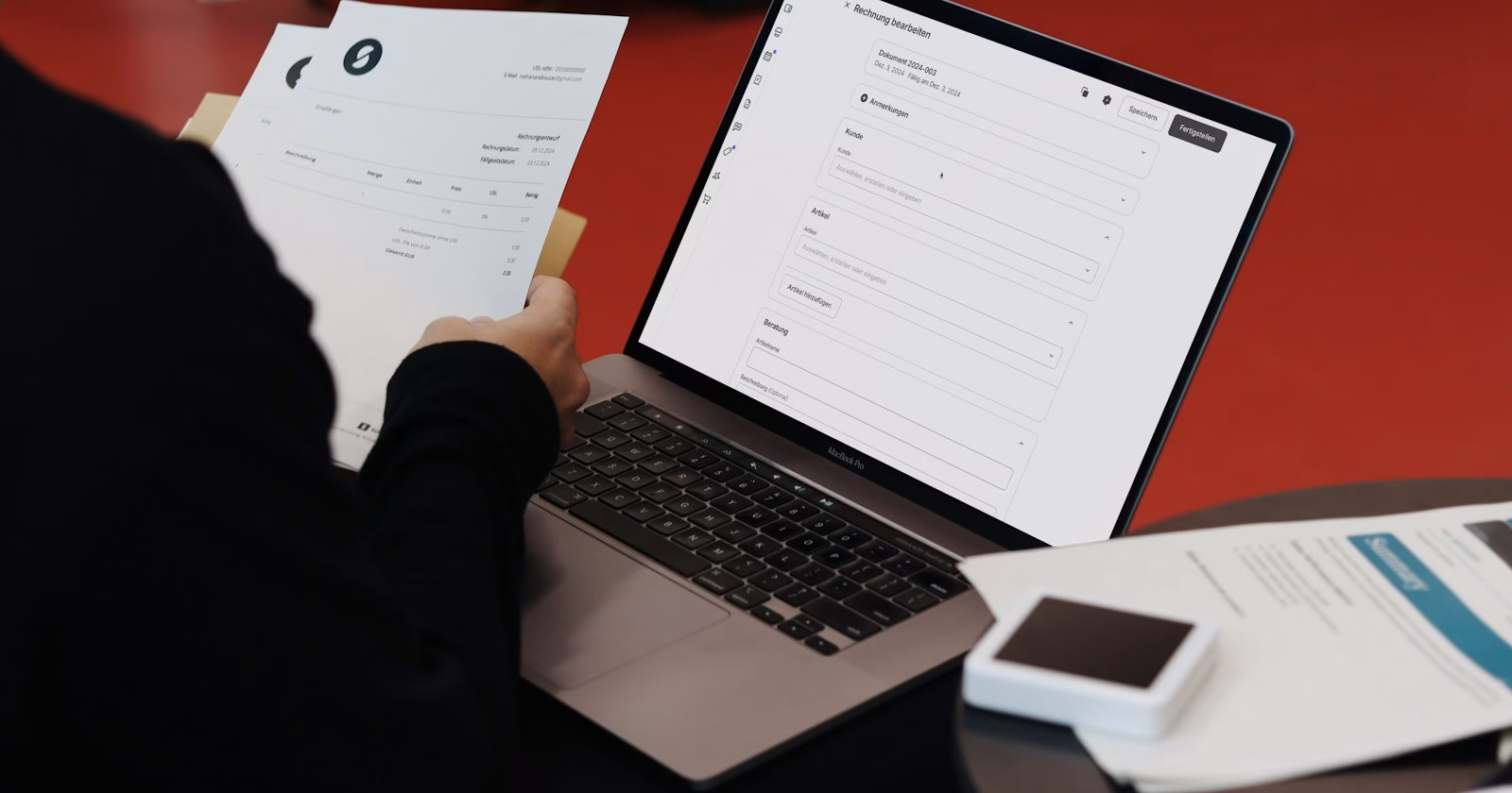 Freelancer checking printed invoices next to a laptop showing an invoice form