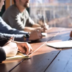 Team members taking notes around a wooden table during a planning meeting