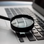 Magnifying glass next to a laptop, representing SEO research tools