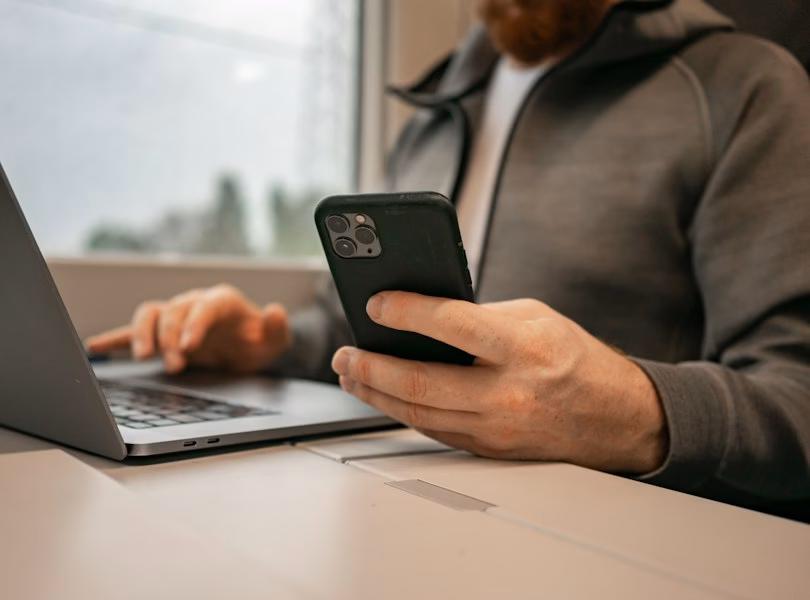 Person replying to a client message on a phone next to a laptop