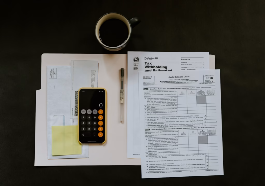 Phone, pen and tax paperwork on a desk, used for adding up Shopify fees and running costs